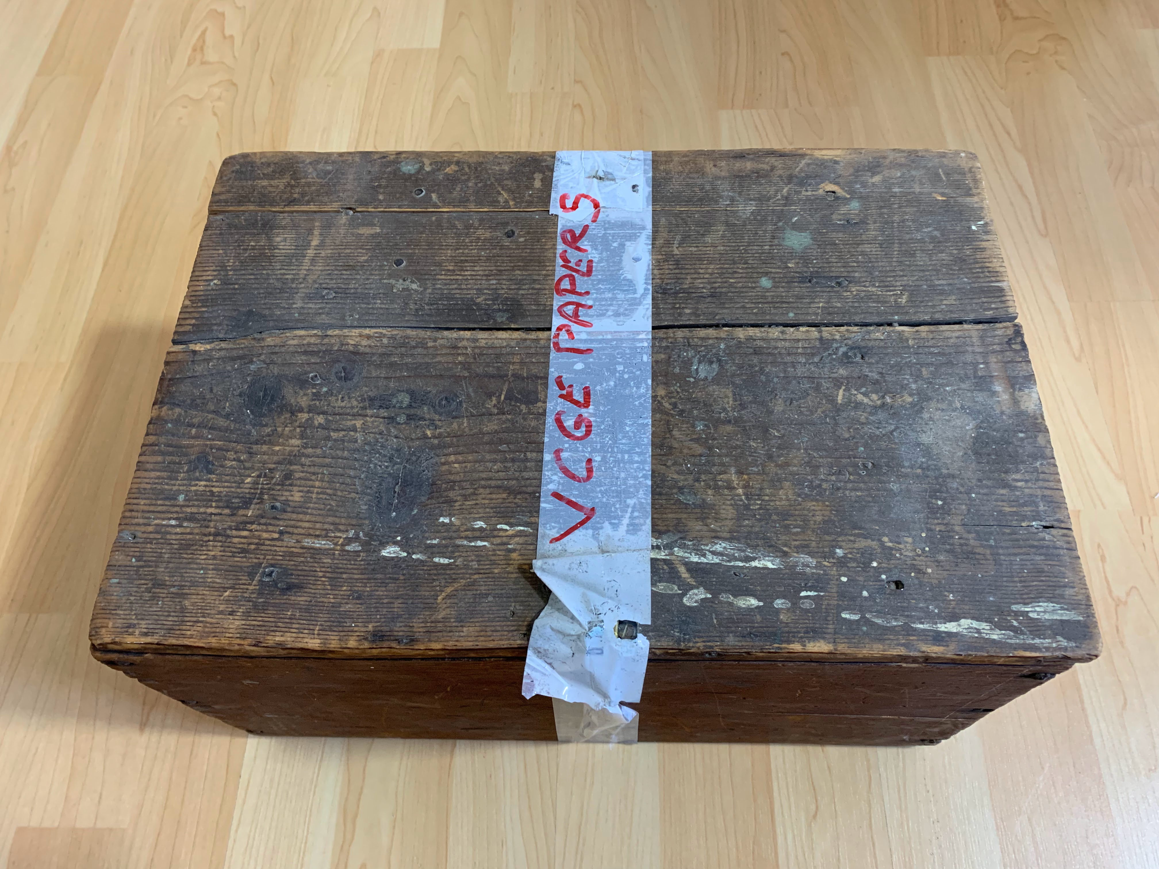 An old wooden box about 50cm x 40cm x 30cm with VGCE papers written in red on white tape stuck to the top.